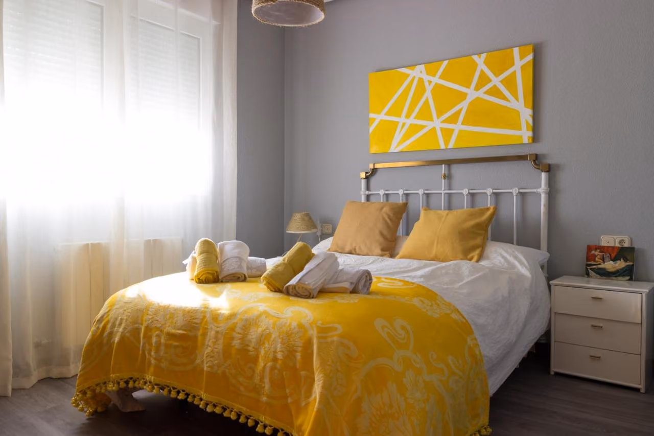Dormitorio con cama doble de forja, colcha amarilla y un cuadro amarillo
