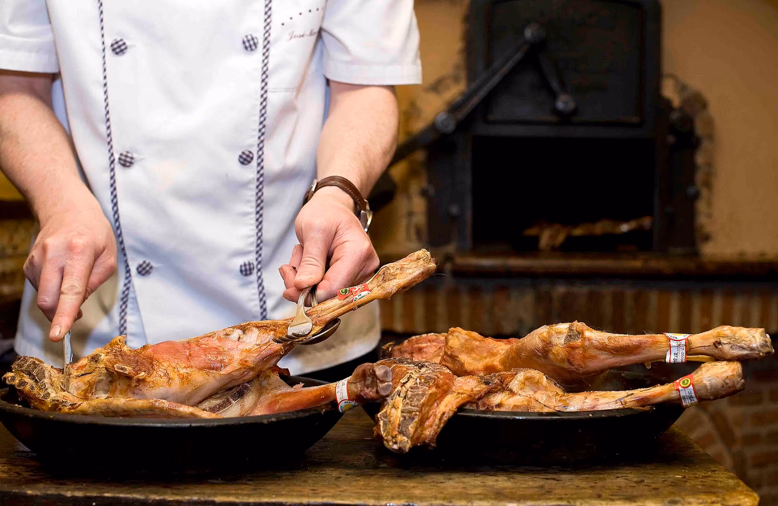 Cocinero sirviendo lechazo asado recién sacado del horno de leña